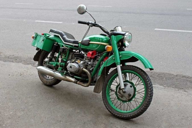 Une moto ancienne verte avec side-car garée sur une route asphaltée, un deux-roues de collection qui nécessite une assurance moto adaptée aux véhicules d'époque.