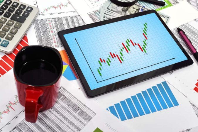 Tablette numérique affichant un graphique boursier en chandeliers au milieu de calculatrices et de billets, illustrant l'exécution de stratégies sur le marché des options