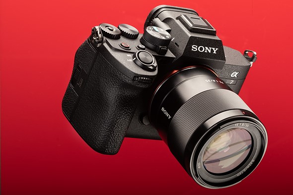 Appareil photo hybride plein format SONY ALPHA 7 IV équipé d'un objectif 35mm, présenté sur un fond rouge vif.