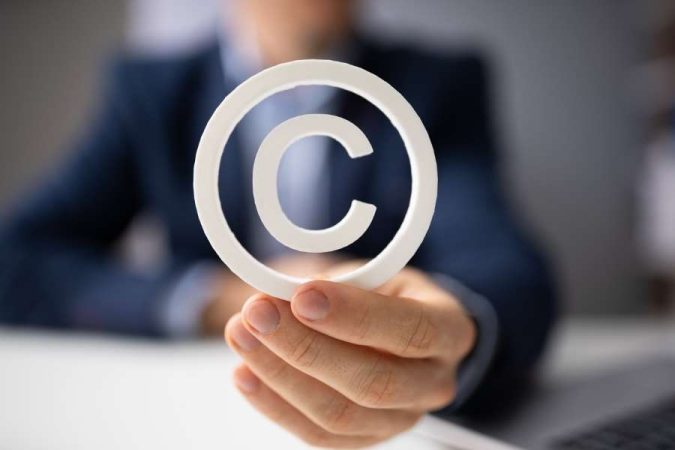 Un homme en costume flou présente au premier plan un grand symbole de copyright blanc entre ses doigts.