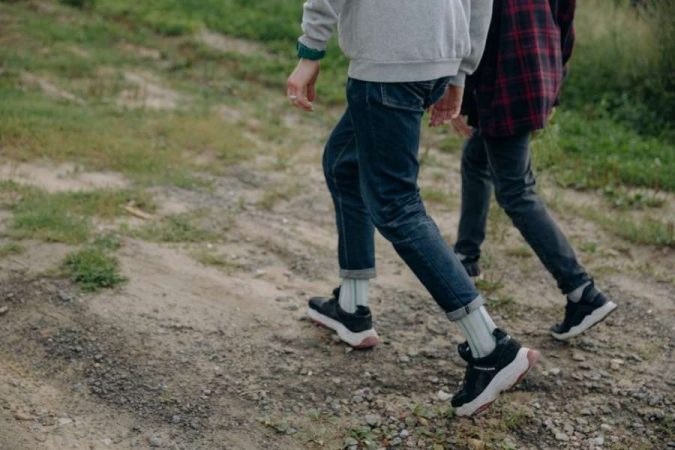 Gros plan sur les jambes de deux personnes marchant activement sur un chemin de terre herbeux, illustrant les bienfaits de la marche pour la santé physique.