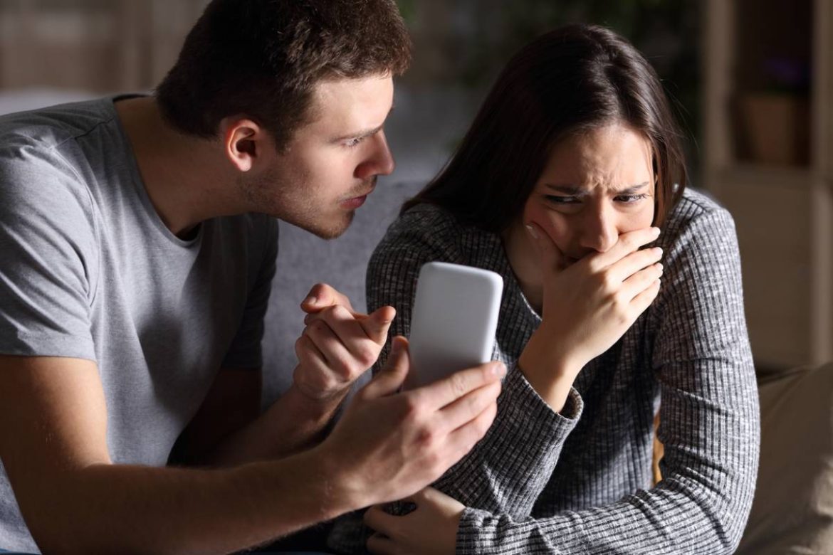 Un homme en colère confrontant une femme en pleurs avec un smartphone, cherchant des preuves d’adultère.
